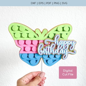 May include: A colorful butterfly cake topper with a pop-it design in green, pink, and blue. The topper has the words "happy birthday" written on it.