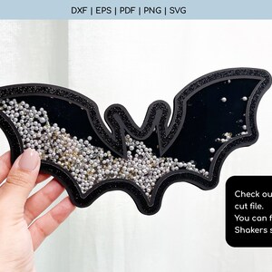K&ouml;nnte beinhalten: Ein schwarzer, fledermausf&ouml;rmiger Shaker mit Glitzerrand. Der Shaker ist mit silbernen und goldenen Streuseln gef&uuml;llt. Der Text "Check our bat shaker cut file. You can find it in our Shakers section." steht auf einem schwarzen Rechteck.