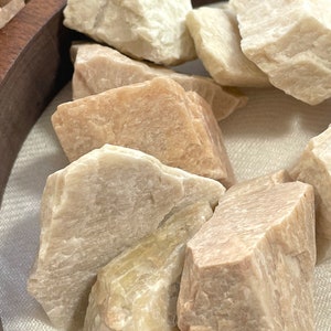 May include: A collection of small, rough-hewn, light brown and white stones. The stones are arranged in a circular wooden bowl.