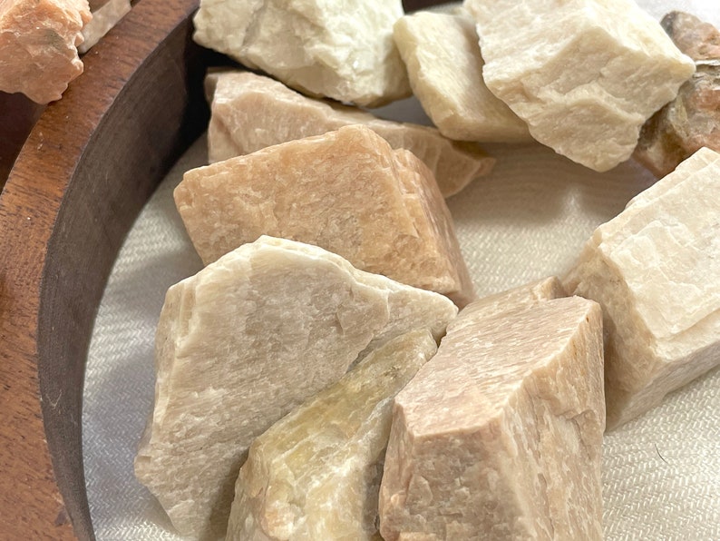 May include: A collection of small, rough-hewn, light brown and white stones. The stones are arranged in a circular wooden bowl.
