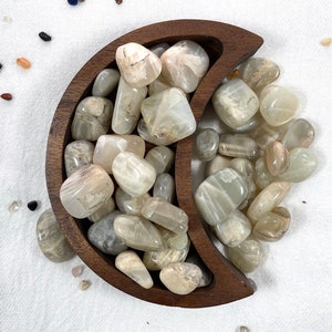 May include: A wooden crescent moon-shaped bowl filled with white and grey sunstone tumbled stones.