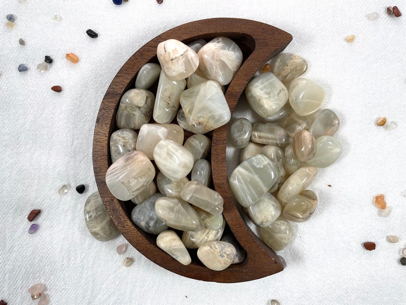 May include: A wooden crescent moon-shaped bowl filled with white and grey sunstone tumbled stones.
