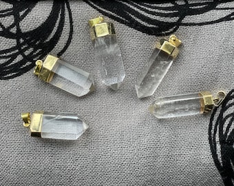 Puede incluir: Cinco puntas de cristal de cuarzo transparente con tapas de metal dorado. Los cristales están dispuestos sobre un fondo de tela gris.