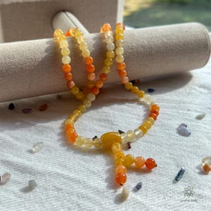 Puede incluir: Un mala o cuentas de oración hechas de cuentas de piedras preciosas amarillas, naranjas y rojas. Las cuentas están enhebradas en un cordón y tienen un borla al final.