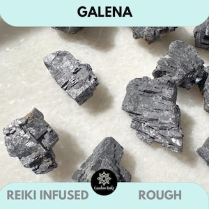 May include: A collection of rough, grey Galena crystals. The crystals are raw and unpolished, with a natural, earthy look. The text "REIKI INFUSED" and "ROUGH" are visible at the bottom of the image.