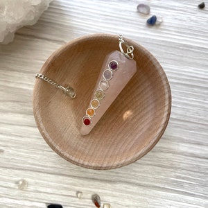 May include: A pink rose quartz pendulum with a silver chain and seven chakra stones. The stones are red, orange, yellow, green, blue, indigo, and violet.