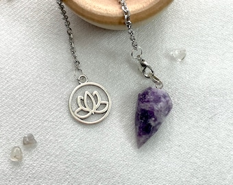 Pode incluir: Um pêndulo de cristal de ametista roxo com uma corrente de prata e um amuleto de prata com um design de flor de lótus.