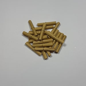 May include: A collection of small, light brown paper scrolls, each tightly rolled and secured in the center with a thin, metallic gold-colored wire ring. The scrolls are arranged in a loose, overlapping pile, showing their cylindrical shape.