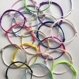 May include: A collection of 20 colorful friendship bracelets made of thin, braided cord. The bracelets are in various colors, including pink, purple, blue, green, yellow, red, white, and black.