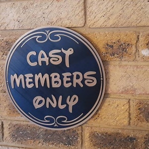 Puede incluir: Un letrero redondo azul y dorado con el texto "CAST MEMBERS ONLY" en una pared de ladrillo.