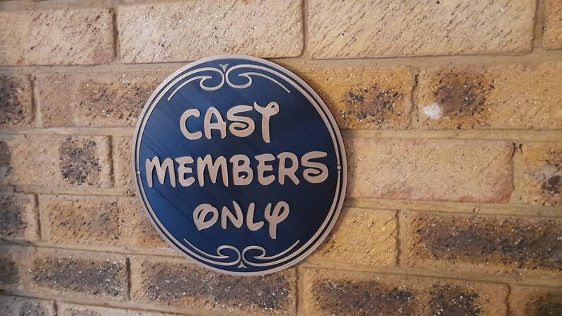 Puede incluir: Un letrero redondo azul y dorado con el texto "CAST MEMBERS ONLY" en una pared de ladrillo.