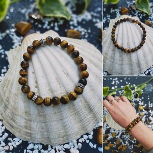 May include: A brown and gold tiger's eye beaded bracelet with silver accents. The bracelet is on a white seashell.