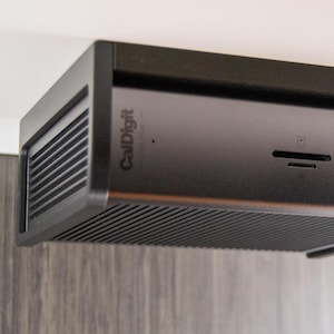 以下が含まれることがあります： USB、USB-C、オーディオジャックなど、複数のポートを備えた黒いCalDigitドッキングステーション。デバイスは、CalDigitのロゴが付いた、溝のあるフロントパネルを備えた洗練された長方形のデザインです。