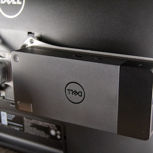 May include: A black Dell monitor stand with a Dell logo and multiple ports. The stand is attached to the back of a monitor.