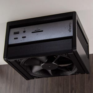 Op de afbeelding: Een zwart en grijs CallDigit computerapparaat met een ventilator. Het apparaat heeft meerdere poorten, waaronder USB en een kaartlezer. Het CallDigit-logo is zichtbaar op het voorpaneel. Het apparaat is aan een muur gemonteerd.