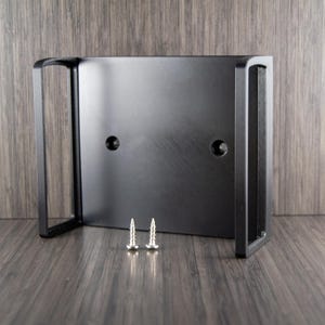 Op de afbeelding: Een zwarte metalen beugel met twee schroefgaten en twee zilveren schroeven. De beugel heeft een rechthoekige vorm met aan elke kant een gebogen handvat. Het product is ontworpen voor montage.