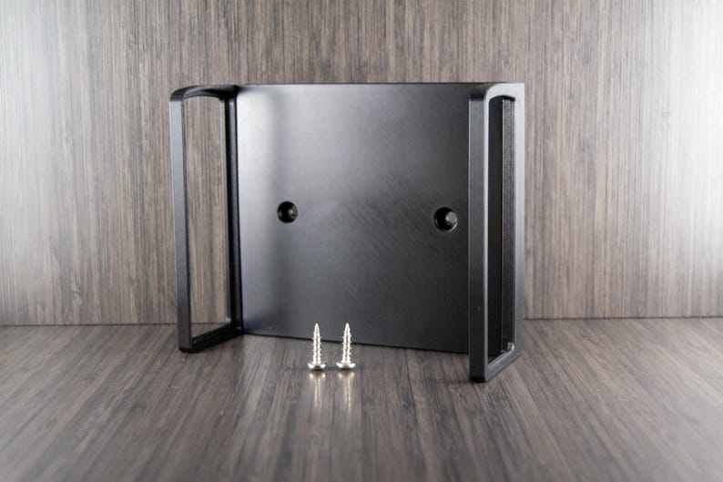 Op de afbeelding: Een zwarte metalen beugel met twee schroefgaten en twee zilveren schroeven. De beugel heeft een rechthoekige vorm met aan elke kant een gebogen handvat. Het product is ontworpen voor montage.