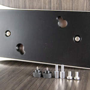 May include: A silver and black metal plate with four holes and a black rubber backing. The plate is accompanied by six screws, two black and four silver.