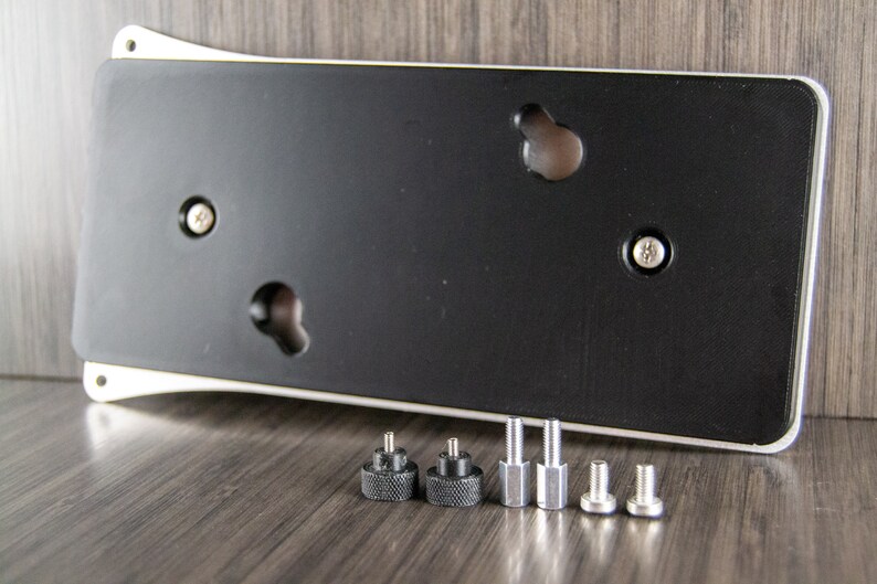 May include: A silver and black metal plate with four holes and a black rubber backing. The plate is accompanied by six screws, two black and four silver.