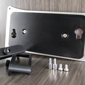 May include: A silver and black wall mount with a black plastic camera mount and four silver screws. The wall mount has a hole for hanging and two screw holes for attaching the camera mount.