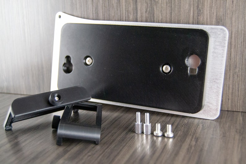 May include: A silver and black wall mount with a black plastic camera mount and four silver screws. The wall mount has a hole for hanging and two screw holes for attaching the camera mount.