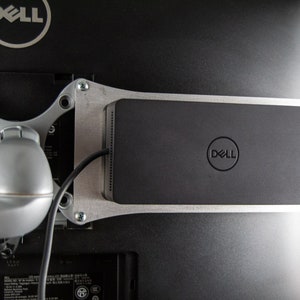 Op de afbeelding: Een zwarte Dell-monitorstandaard met een zilveren metalen frame en een Dell-logo aan de voorkant. De standaard is bevestigd aan de achterkant van een Dell-monitor.