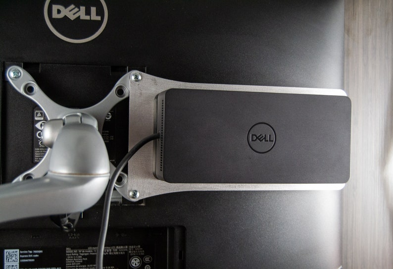 May include: A black Dell monitor stand with a silver metal frame and a Dell logo on the front. The stand is attached to the back of a Dell monitor.