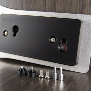 May include: A silver and black metal plate with two holes for mounting. The plate is accompanied by six screws, two black and four silver.