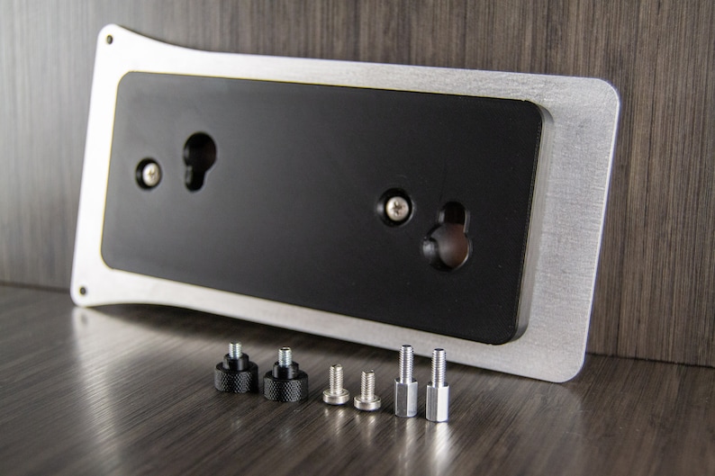 May include: A silver and black metal plate with two holes for mounting. The plate is accompanied by six screws, two black and four silver.