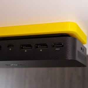 May include: A black computer with multiple ports on the back is mounted to the underside of a yellow shelf.