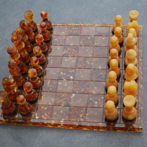 Könnte beinhalten: Ein Schachspiel mit bernsteinfarbenen Figuren auf einem braunen und weißen Schachbrett. Das Brett besteht aus einem durchscheinenden Material mit einem gesprenkelten Muster.
