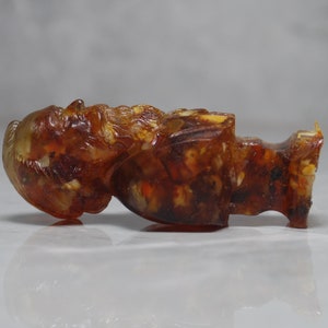 May include: A small amber figurine of a person with a beard. The figurine is carved in detail and has a warm, honey-colored hue.
