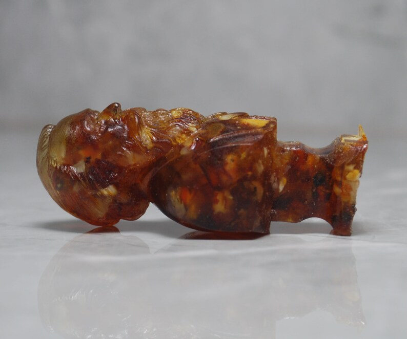 May include: A small amber figurine of a person with a beard. The figurine is carved in detail and has a warm, honey-colored hue.