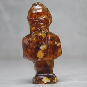 May include: A bust sculpture of a person with a beard made of amber. The sculpture is detailed with intricate carvings and has a warm, golden hue.