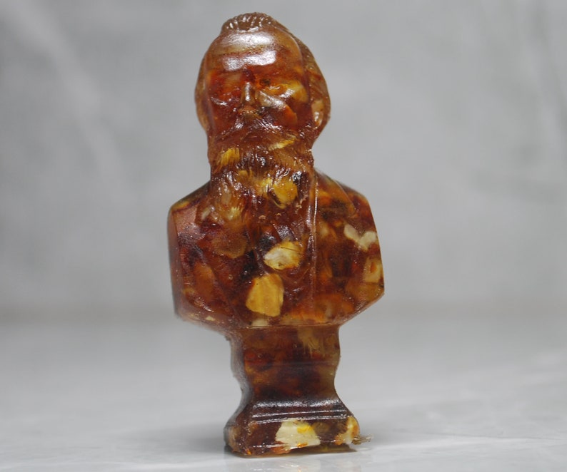 May include: A bust sculpture of a person with a beard made of amber. The sculpture is detailed with intricate carvings and has a warm, golden hue.