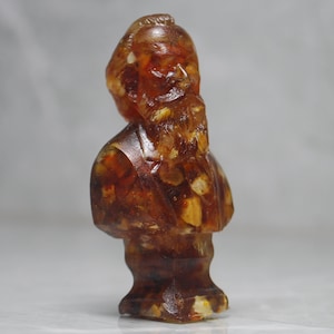 May include: A bust sculpture of a person with a beard made of amber. The sculpture is a dark brown color with flecks of gold and white.