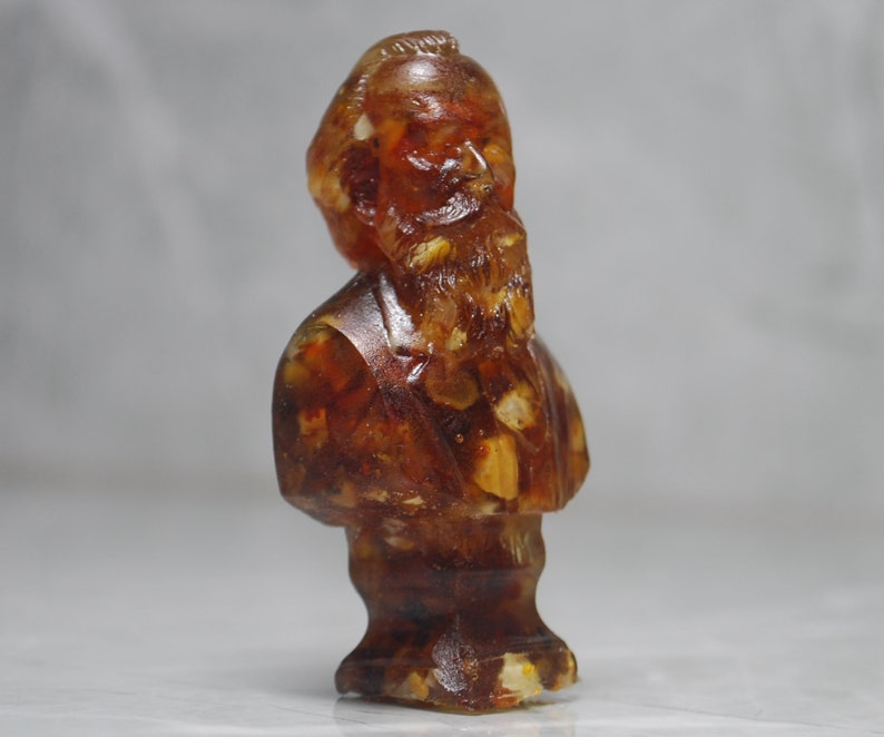 May include: A bust sculpture of a person with a beard made of amber. The sculpture is a dark brown color with flecks of gold and white.