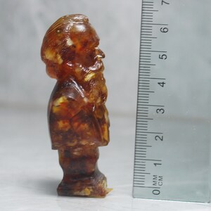 May include: A small amber figurine of a man with a beard, standing approximately 5 cm tall.