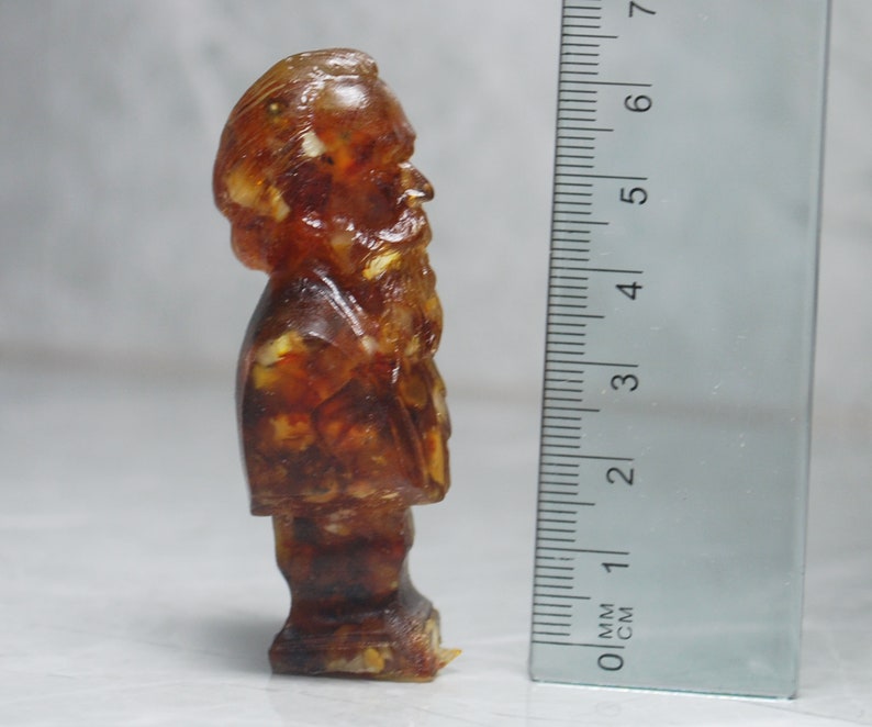 May include: A small amber figurine of a man with a beard, standing approximately 5 cm tall.