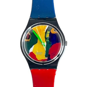 Puede incluir: Un reloj con un diseño abstracto colorido con una correa de plástico negra, azul y roja. La esfera del reloj presenta un diseño abstracto amarillo, verde, rojo, azul y blanco. La esfera del reloj también incluye el texto "Swatch Swiss".