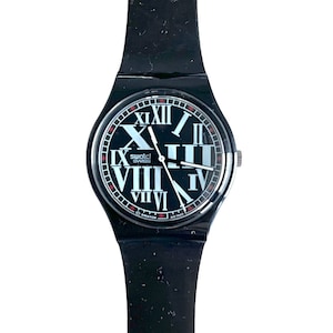 May include: Black Swatch watch with a black plastic strap and a black face with white Roman numeral hour markers. The watch face also has the word "swatch" and "swiss" printed in white.