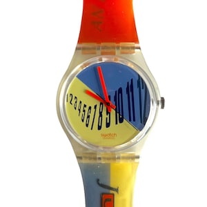 May include: A vintage Swatch watch with a clear plastic case and a colorful band. The watch face is divided into two sections, one yellow and one blue, with black numbers and an orange hour hand.