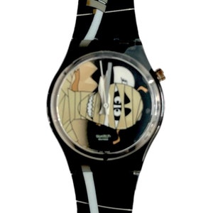 Op de afbeelding: Een zwart-witte Swatch-horloge met een mummie-ontwerp op de wijzerplaat. Het horloge heeft een zwarte plastic band met een wit en grijs patroon.