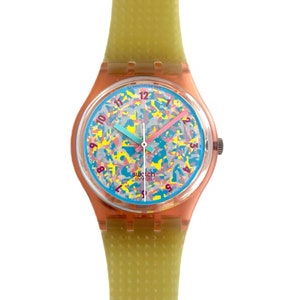 Op de afbeelding: Een kleurrijk Swatch-horloge met een lichtblauwe wijzerplaat en een abstract patroon in groen, roze en geel. Het horloge heeft een groene plastic band.