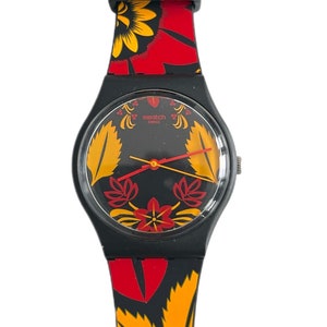 Pode incluir: Relógio Swatch preto com mostrador preto e pulseira com estampa floral vermelha e amarela. O mostrador do relógio tem a palavra "swatch" e "swiss" impressa.