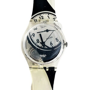 May include: A white and black Swatch watch with a clear plastic case and a black and white patterned strap. The watch face is white with black numbers and hands. The watch says "Swatch Swiss" on the face.