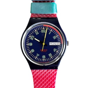 May include: A blue and red Swatch watch with a blue face and a red and white striped strap. The watch face has a date window that says "MON 12".