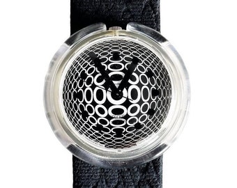 May include: A black and white watch with a clear plastic case and a black fabric band. The watch face has a pattern of overlapping circles.