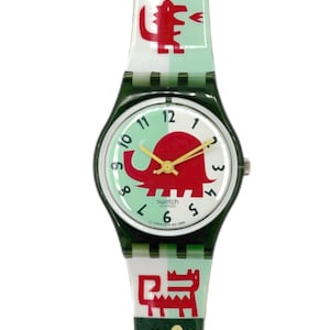 May include: A Swatch watch with a green and white strap featuring red cartoon animal designs. The watch face is white with a red elephant graphic and yellow hands. The watch has a dark green case.