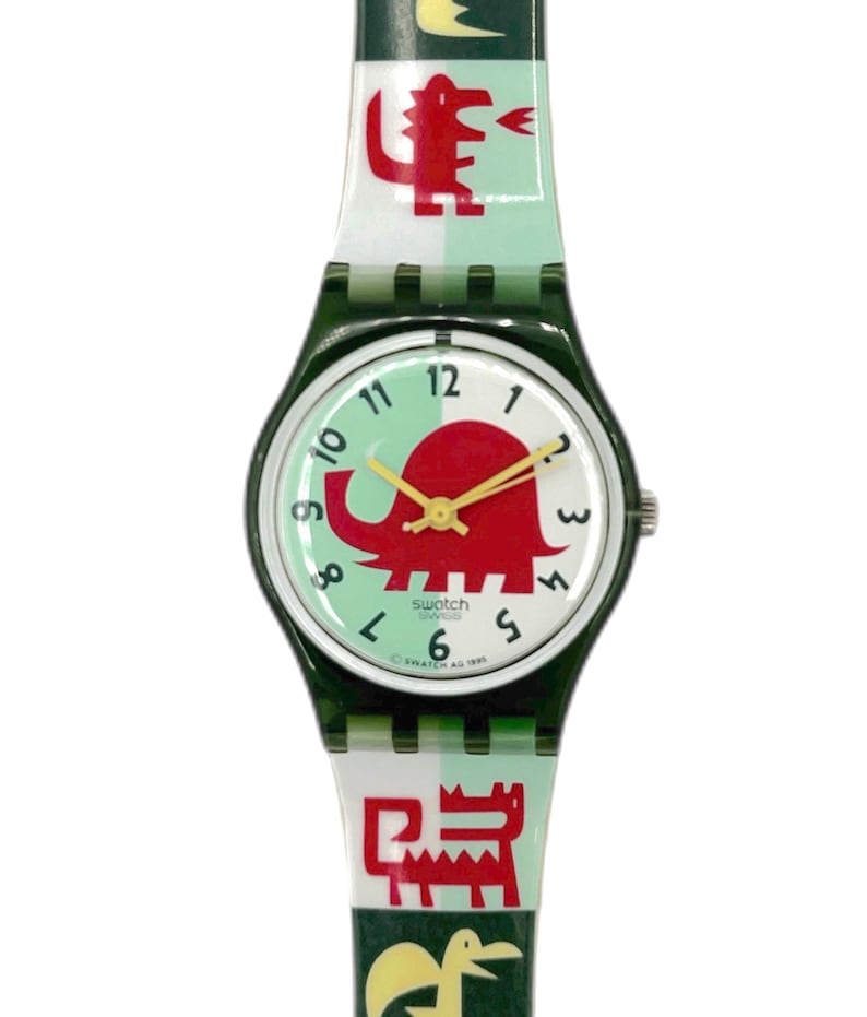 May include: A Swatch watch with a green and white strap featuring red cartoon animal designs. The watch face is white with a red elephant graphic and yellow hands. The watch has a dark green case.